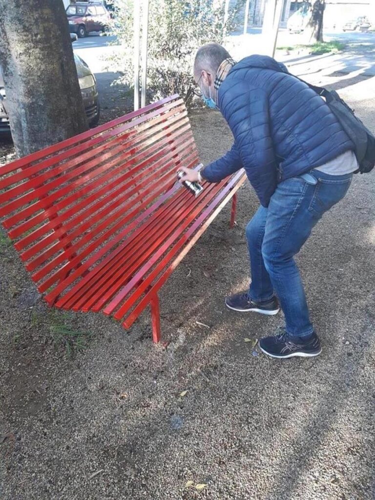 Il consigliere Sottocornola ripristina la vernice di una panchina rossa che era stata vandalizzata.